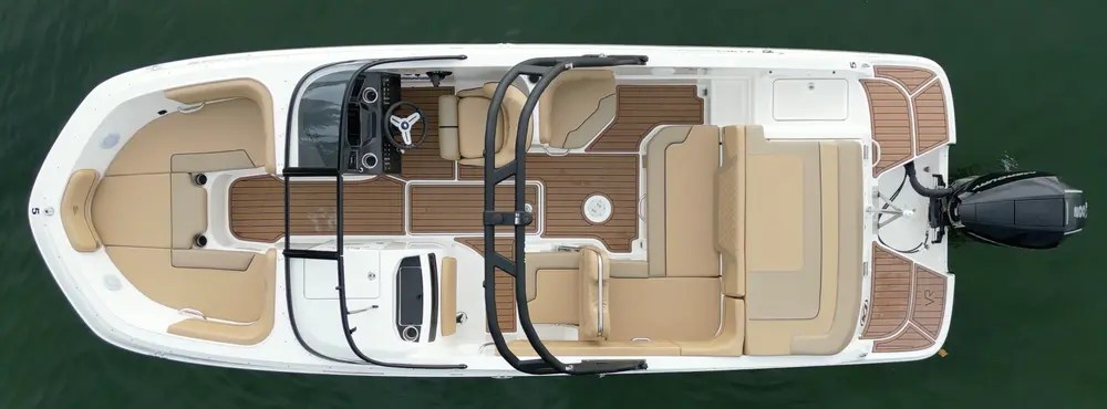 Overhead view of a white boat with tan seating and wooden deck on water.