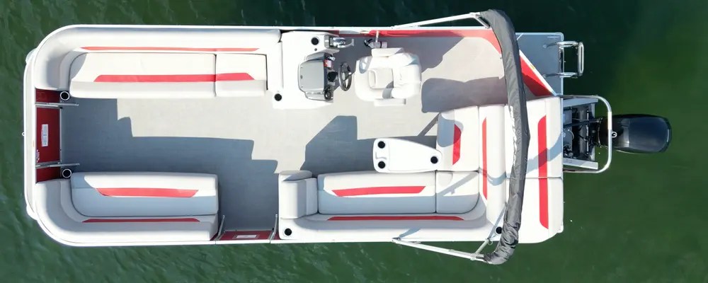 Aerial view of a white and red pontoon boat on green water.