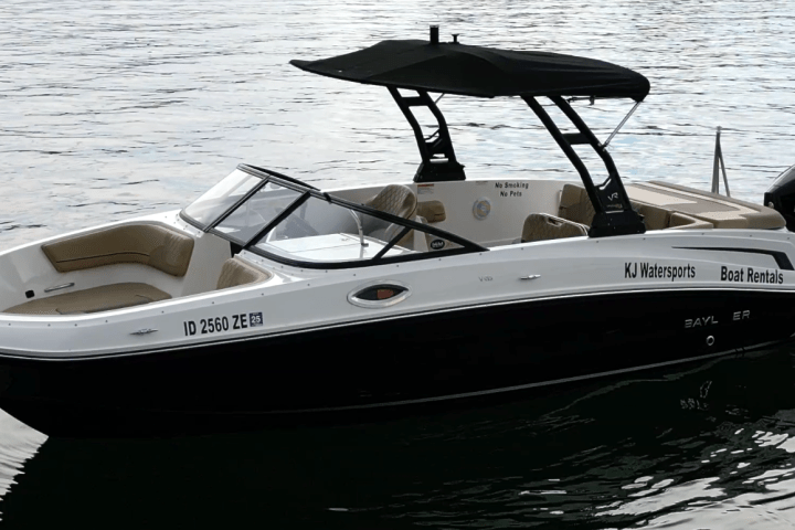 Black and white motorboat with canopy on calm water, labeled 'KJ Watersports Boat Rentals'.