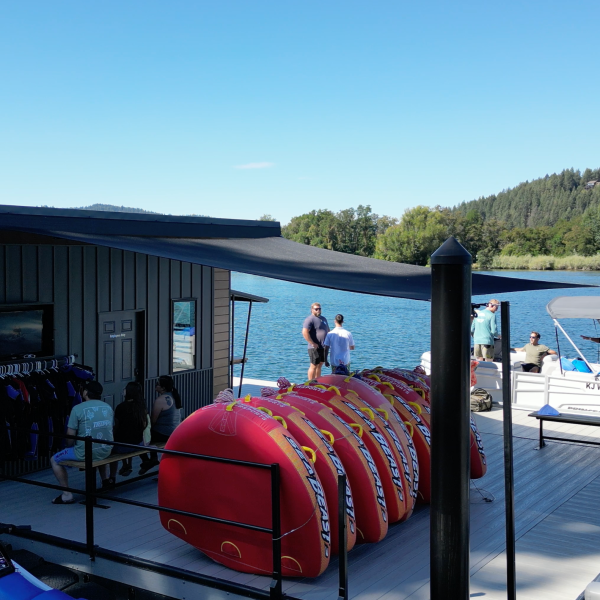 Dock with water sports equipment and boats, people standing nearby, and a lake in the background.