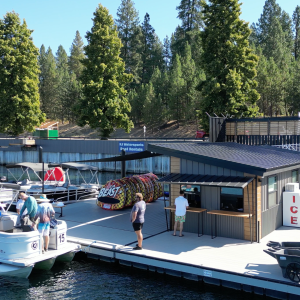 People on a boat docked at a lakeside marina with trees in the background.