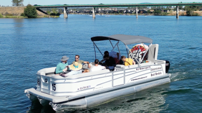 Pontoon boat with several people on a river near a bridge, under a clear sky.
